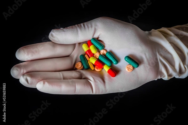 Obraz Mountain of pills in the hand of a doctor in a white glove on an isolated black background