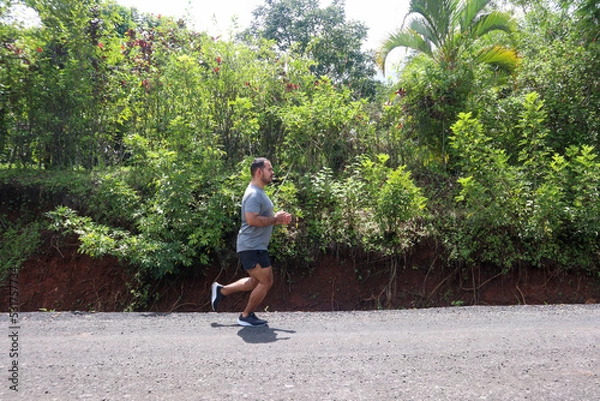 Fototapeta Young mid weight man jogging on the unpaved road with green background