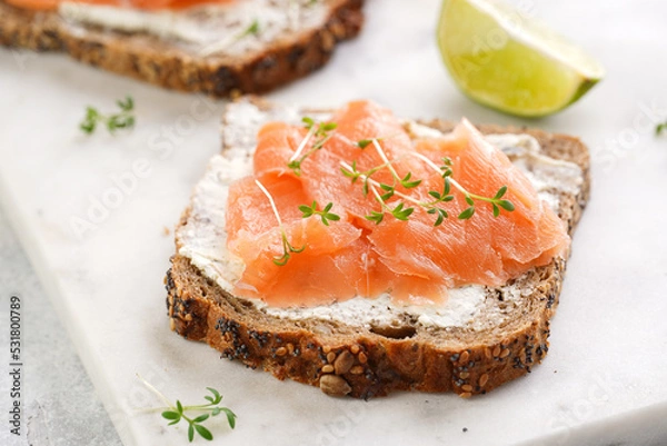 Obraz Wholewheat bread sandwiches with cream cheese and smoked salmon on marble board with lime slices and sour cream
