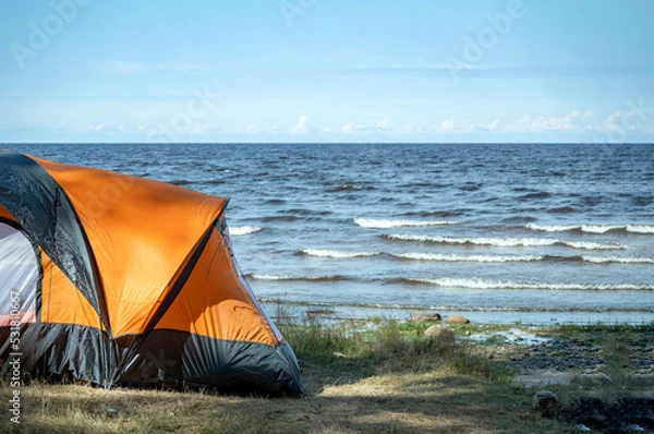 Fototapeta The edge of a tourist tent on the shore against the background of the exciting sea. Camping, camping, survival in the wild, outdoor living.