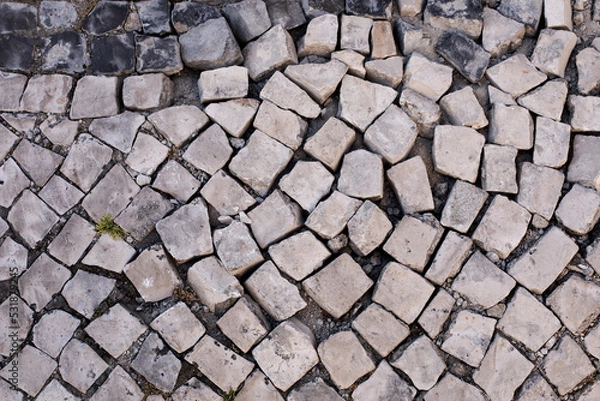 Fototapeta Trottoir pavé dans un état de délabrement où les cubes de pierre sont disjoints. Rue d'une ville aux maisons en ruine.