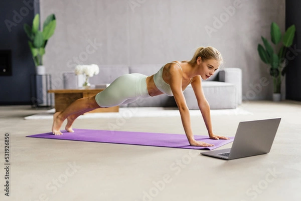 Obraz Fit young woman planking on exercise mat at home in the living room