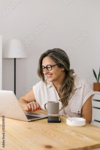 Fototapeta Smiling woman having online meeting at home via laptop