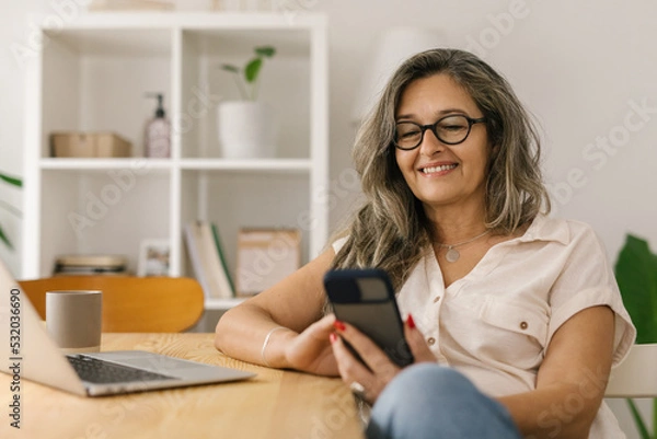 Fototapeta Happy woman sitting and using smart phone at home