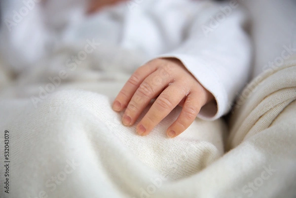 Fototapeta Small hand of a newborn baby with thin skin and long nails. The baby's hand lies on a light soft blanket in the cradle.