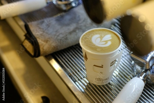 Fototapeta coffee latte or cappuccino with latte art on top in paper take away cup well prepare by barista in small cafe at espresso machine