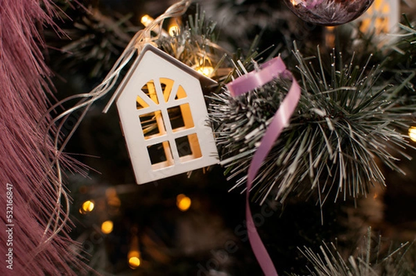 Fototapeta garland with a toy in the form of a white house on a Christmas tree with a blurred background