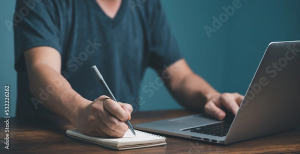 Fototapeta E learning concept. Casual business man studying online course via laptop computer and writing on notebook.