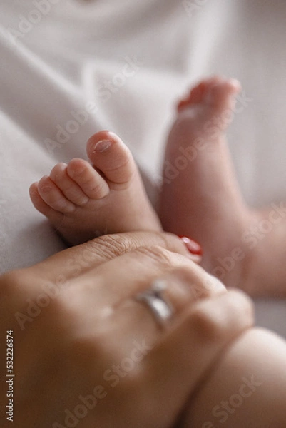 Fototapeta Mother holding newborn baby feet in hands. Mom taking care about infant child after taking bath.