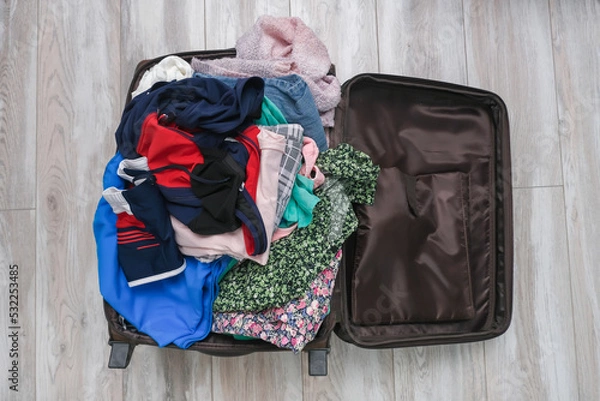 Fototapeta Open suitcase on the floor with a messy pile of clothes, getting away from home in a hurry