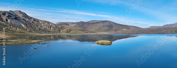 Obraz A beautiful landscape in Iceland of mountains, a bright blue and blue sky of light clouds, reflected in  huge flat surface of a reservoir.