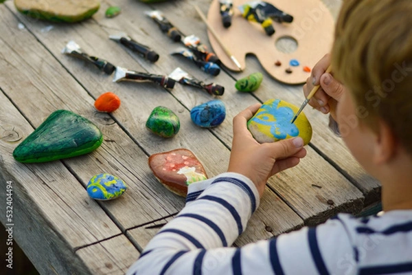 Fototapeta A detailed picture of a child's hands drawing a fungus on a stone with acrylic paints. Home hobbies are authentic. Artwork on stones.