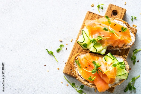 Obraz Open sandwich with cream cheese, salmon and cucumber. Top view at white table.