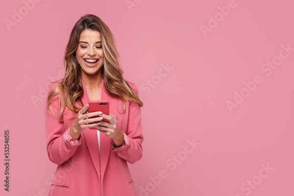 Obraz Photo of a happy young beautiful woman using mobile phone, smiling, posing isolated over pink pastel background.