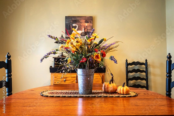 Obraz dinning room decorated for fall with flower bouquet centerpiece and pumpkins on oak table