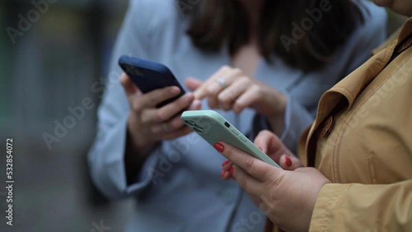 Obraz Close up focus on females hands using phones. Two women with smartphones on the street, the girl explains, shows, tells, demonstrates, gesticulates with her hand
