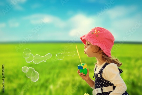 Fototapeta Little girl playing with soap bubbles outdoor in green field