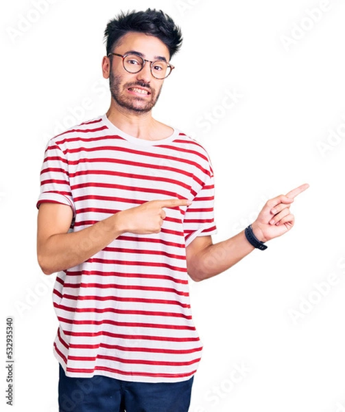 Fototapeta Young hispanic man wearing casual clothes pointing aside worried and nervous with both hands, concerned and surprised expression