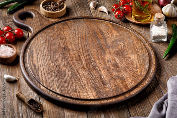 Fototapeta Empty round wooden cutting board for food, pizza. Menu, recipe Mock up. Wooden background with oil, tomatoes and spices. .