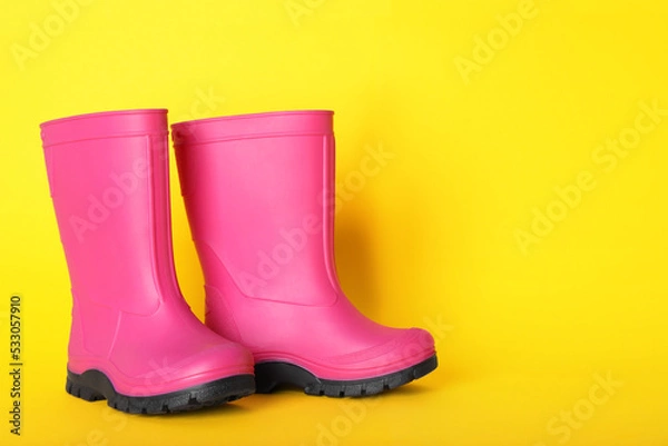 Fototapeta Pair of bright pink rubber boots on yellow background. Space for text