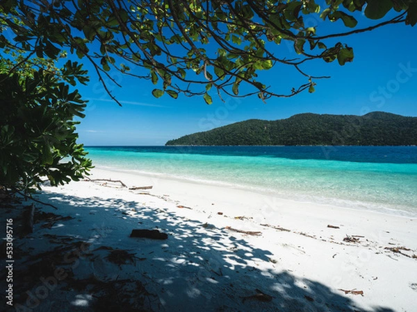 Fototapeta Scenic view of Koh Ra Wi Island white sand beach, clear turquoise sea against summer blue sky with Koh Adang Island background and tree shade foreground. Near Koh Lipe Island, Satun, Thailand.
