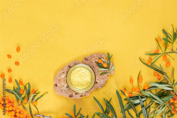 Fototapeta Jar with sea buckthorn cream on stone and yellow background, with space for text.