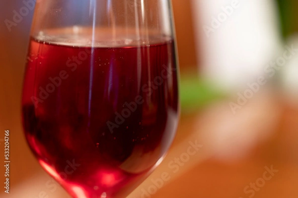 Fototapeta Wine glass with red raspberry juice, cut with water on orange ple with an accent of green - an interesting background