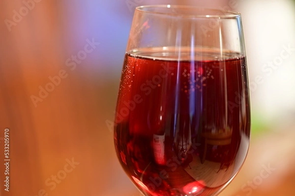 Fototapeta Wine glass with red raspberry juice, cut with water on orange ple with an accent of green - an interesting background
