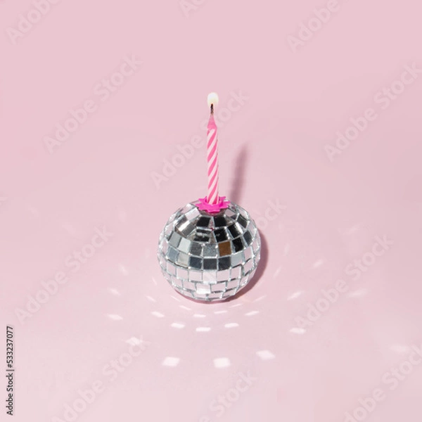 Fototapeta Shiny disco ball and candle on pastel light pink background. Minimalistic party concept. Creative birthday composition.