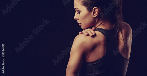 Obraz Strong sporty woman doing hands the massege to relax the tension in shoulder and scapula in sport bra top on empty copy space black studio background. Sports injury. Closeup toned portrait. Back view.