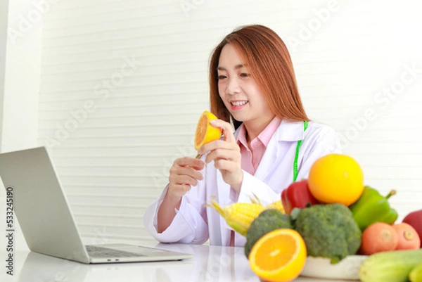 Obraz Asian female doctor or nutritionist Consulting the patient about the diet There were various fruits and vegetables lying on the white table. online patient health care concepts, healthy eating.