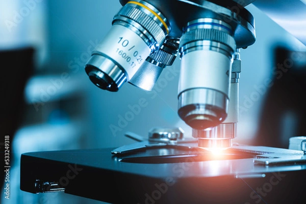 Fototapeta close up of compound microscope with ray of orange light shining in lab setting