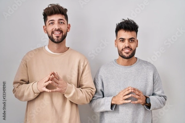 Fototapeta Young homosexual couple standing over white background hands together and fingers crossed smiling relaxed and cheerful. success and optimistic