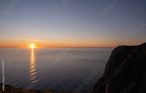 Fototapeta Wonderful landscapes in Norway. Nord-Norge. Beautiful scenery of a midnight sun sunset at Nordkapp (Cape North). Boat and globe on a cliff. Rippled sea and clear orange sky. Selective focus