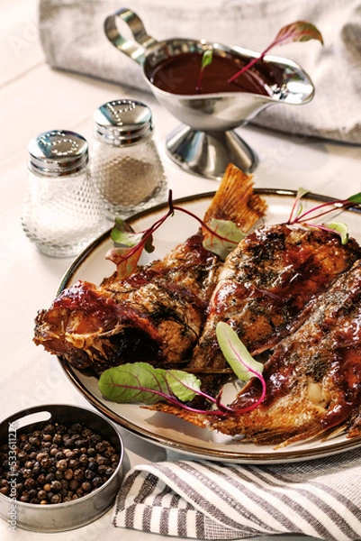 Fototapeta Baked sea bass with herbs and sauce, three fish on a platter, homemade table setting, cozy and warm