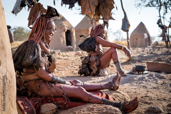 Obraz Kobiety Himba siedzące przed ich chatami w tradycyjnej wiosce Himba w pobliżu Kamanjab, północna Namibia, Afryka.