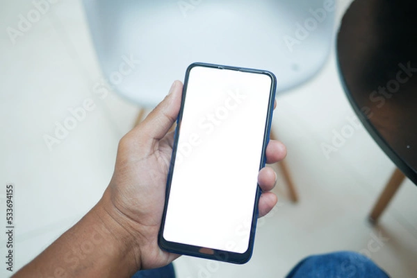 Fototapeta POV of young man hand using smart phone with empty screen sitting on chair 