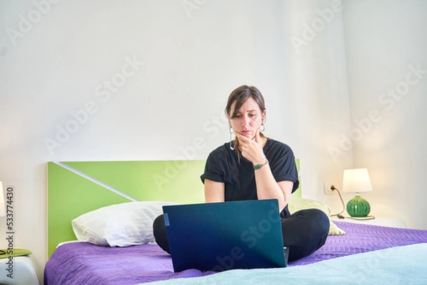 Fototapeta Caucasian pensive woman looking at computer from bedroom