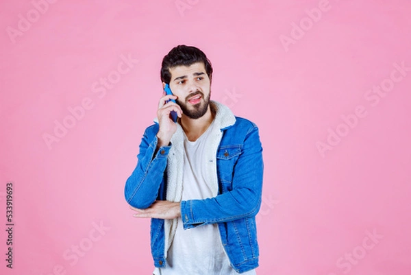 Obraz Young man in casual blue jacket and white shirt holding a smartphone against a pink background, capturing a selfie or taking a photo, with a modern and vibrant aesthetic