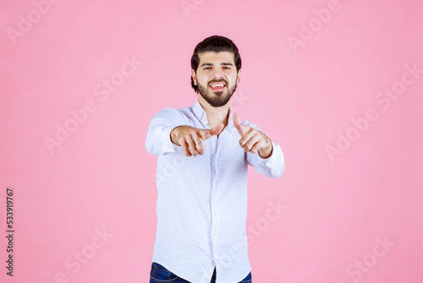 Obraz A person with a blurred face stands against a pink background, wearing a white shirt and holding a string or object in their hands, creating a playful or casual scene.