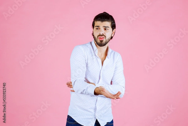 Obraz Young man with crossed arms posing against a pink background, casual style with white shirt and dark pants, modern portrait with a vibrant and clean aesthetic