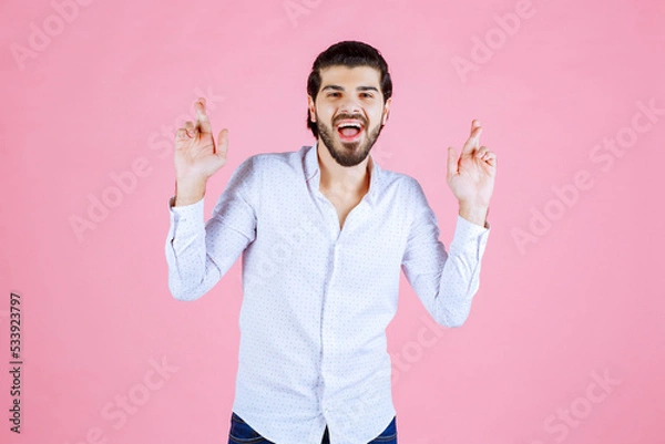 Obraz A young man in a white shirt standing against a pink background with hands raised in a gesture of excitement or celebration