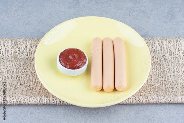 Fototapeta Boiled sausage and ketchup on yellow plate