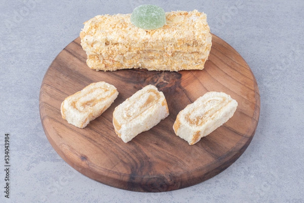Fototapeta Cake roll and slice on a wooden board on marble background
