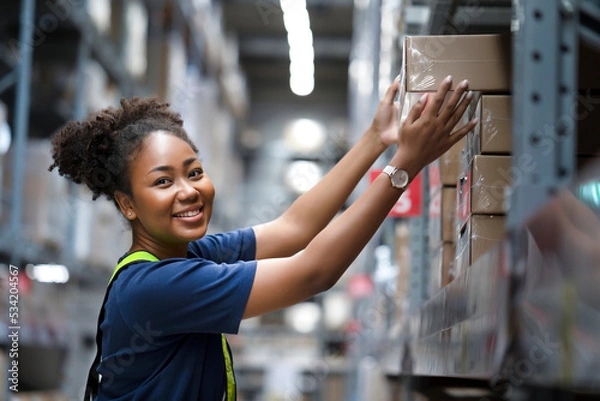 Fototapeta African American warehouse worker take flat box from shelf in big warehouse factory, Online shopping store for logistic service to deliver the shipment, check barcode before passing to transportation