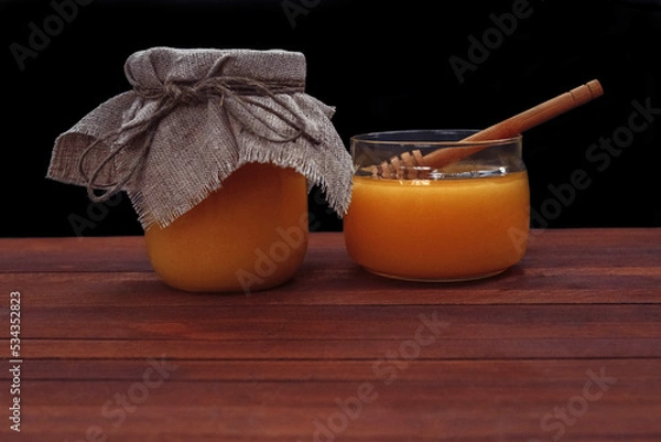 Fototapeta Honey in a glass jar with a spoon with a film effect, grain, noise out of focus on a brown wooden table with an empty space for text, close-up, dessert concept, healthy nutrition, health and immunity