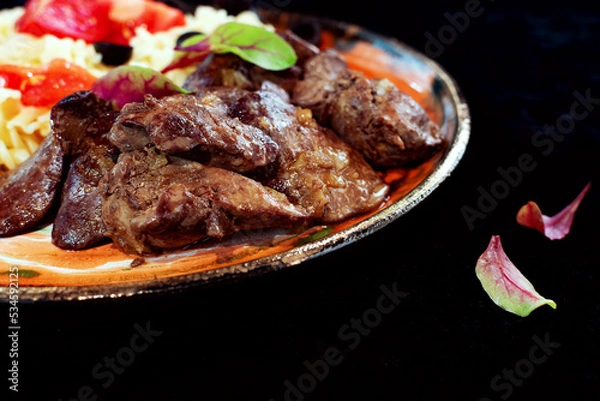 Fototapeta Fried chicken liver, juicy soft and tender meat with young beet leaves on a black background on the side, empty space