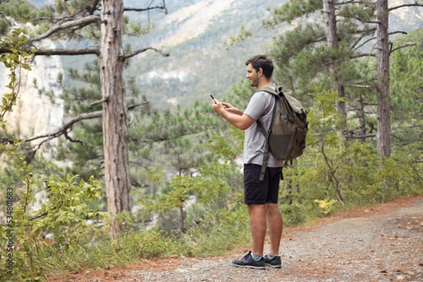 Fototapeta Full body tourist man with backpack in the mountain forest using mobile phone, looking for connection