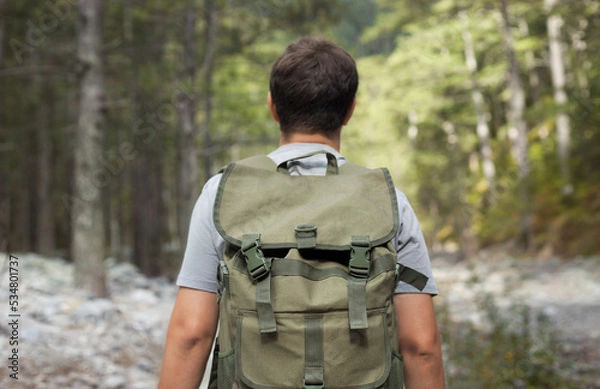 Fototapeta Close up hiking man from behind with his tourist backpack is walking in a forest. Healthy lifestyle concept.