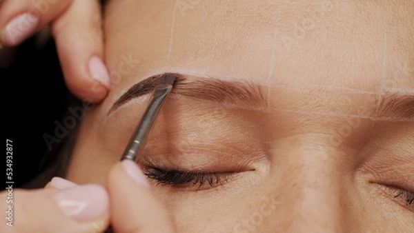 Fototapeta Woman is  on the Eyebrow coloring procedure. Professional lamination procedures of female eyebrows in beauty salon. Closeup view of client face and stylist's hands working.  Beauty care concept.